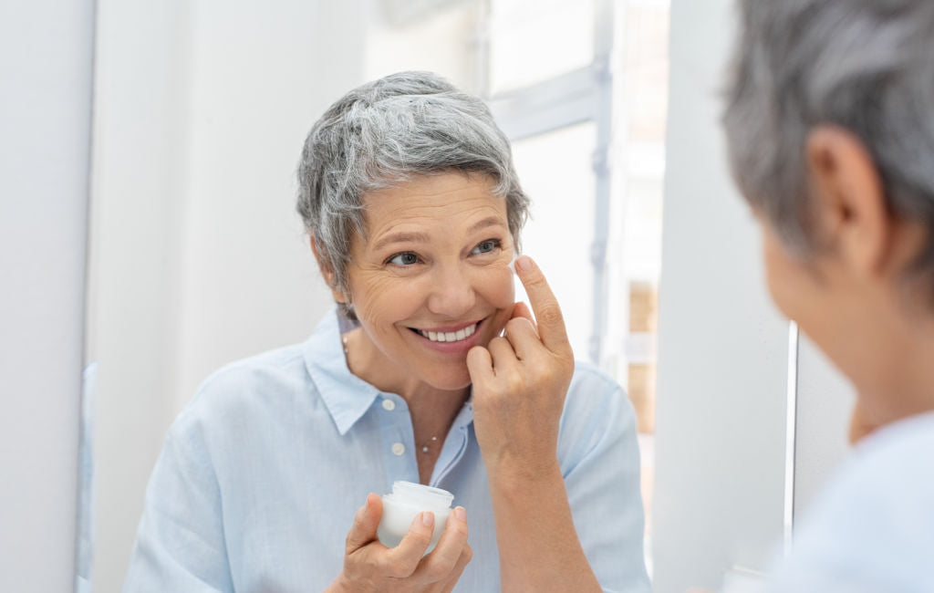 older woman putting on skin cream at mirror