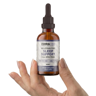 Hand holding a bottle of Zebra CBD Sleep Support supplement on a white background